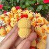 A hand holds a yellow crocheted animal keychain with orange accents, surrounded by other similar items.