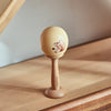 A wooden bear musical instrument set featuring a spherical head and a wooden handle, resting on a light wood surface.