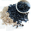 A pile of small black plastic safety eyes for crafting, some in a white bowl and scattered on paper.