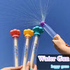 Une main tient une pistolet à eau transparente avec une buse violette, projetant de l'eau dans le ciel bleu.