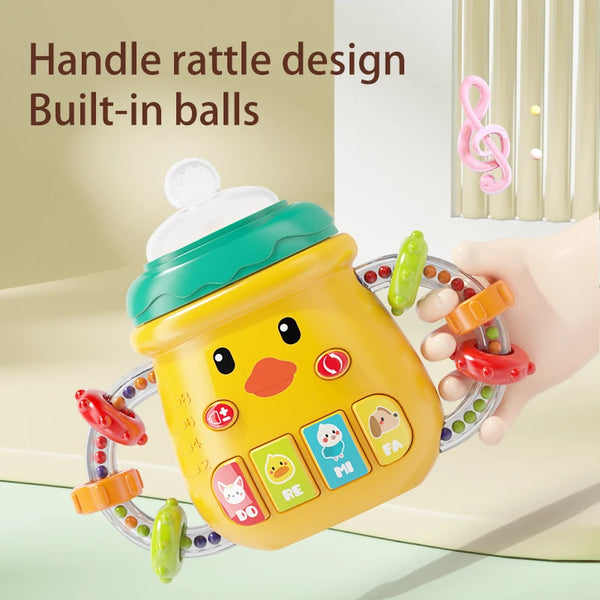 A yellow musical feeding bottle and teether with built-in balls is held by a hand.