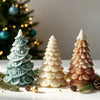 Three white silicone candle molds shaped like Christmas trees with star and snowflake details on a white surface.
