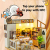 A miniature tea house display featuring a wooden dollhouse kit and NFC technology for personalized stories.