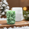 A green silicone candle mold shaped like dragons and clouds sits on a wooden surface next to a white candle.