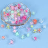 A mix of colorful acrylic beads in pink, green, and clear tones is displayed in a shallow dish for DIY jewelry making.