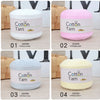 Four rolls of 100% cotton yarn in white, pink, gray, and yellow displayed on a wooden surface.