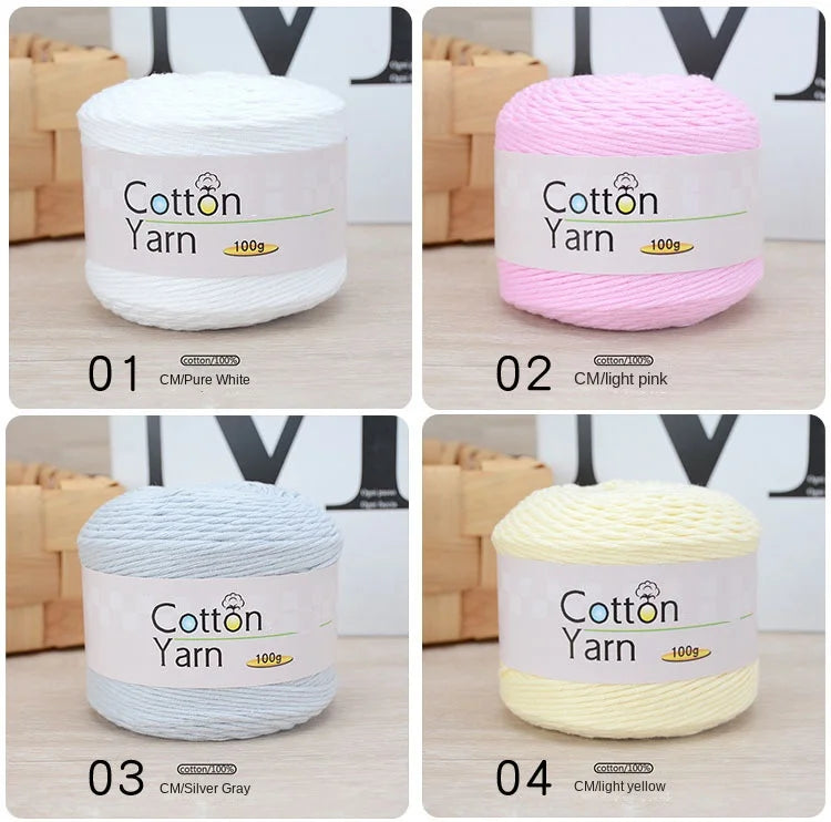 Four rolls of 100% cotton yarn in white, pink, gray, and yellow displayed on a wooden surface.
