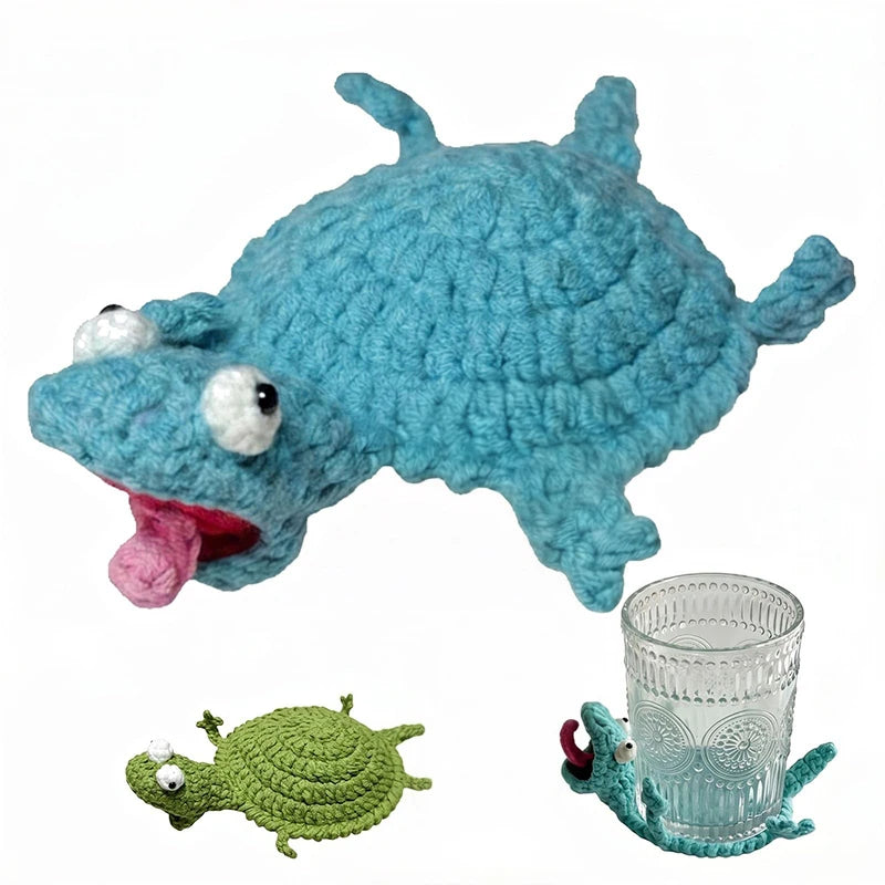 A handmade blue crochet lizard figurine resting next to a small green crochet lizard and a glass coaster.