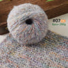 A ball of soft alpaca blend yarn labeled #07 in a multicolored mix resting on a knitted fabric.