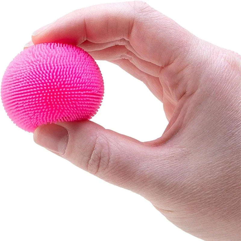 A hand is holding a bright pink, textured fuzz ball sensory toy.