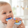 A baby is holding a blue lion-shaped silicone teether with remote control features.