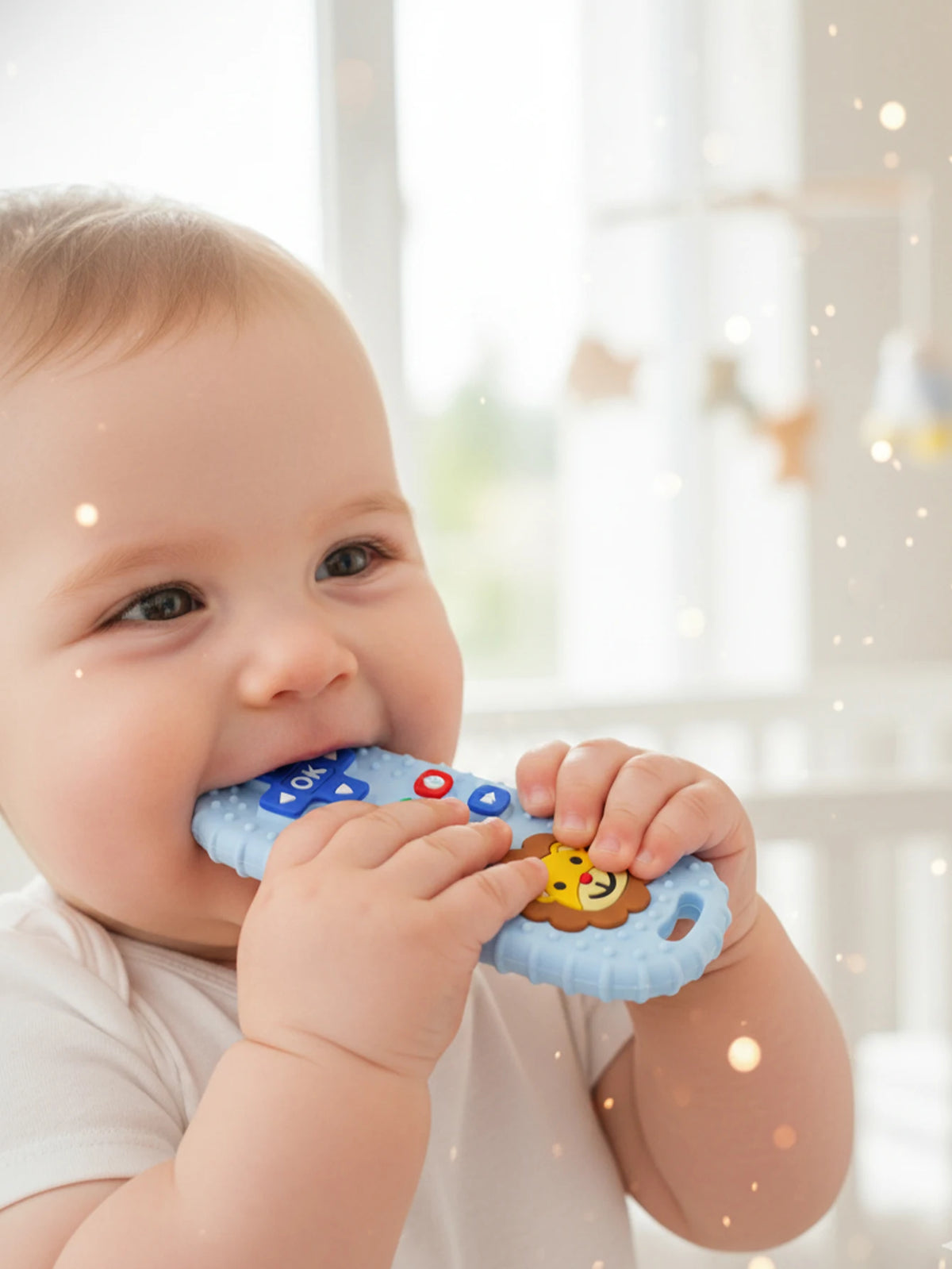 A baby is holding a blue lion-shaped silicone teether with remote control features.