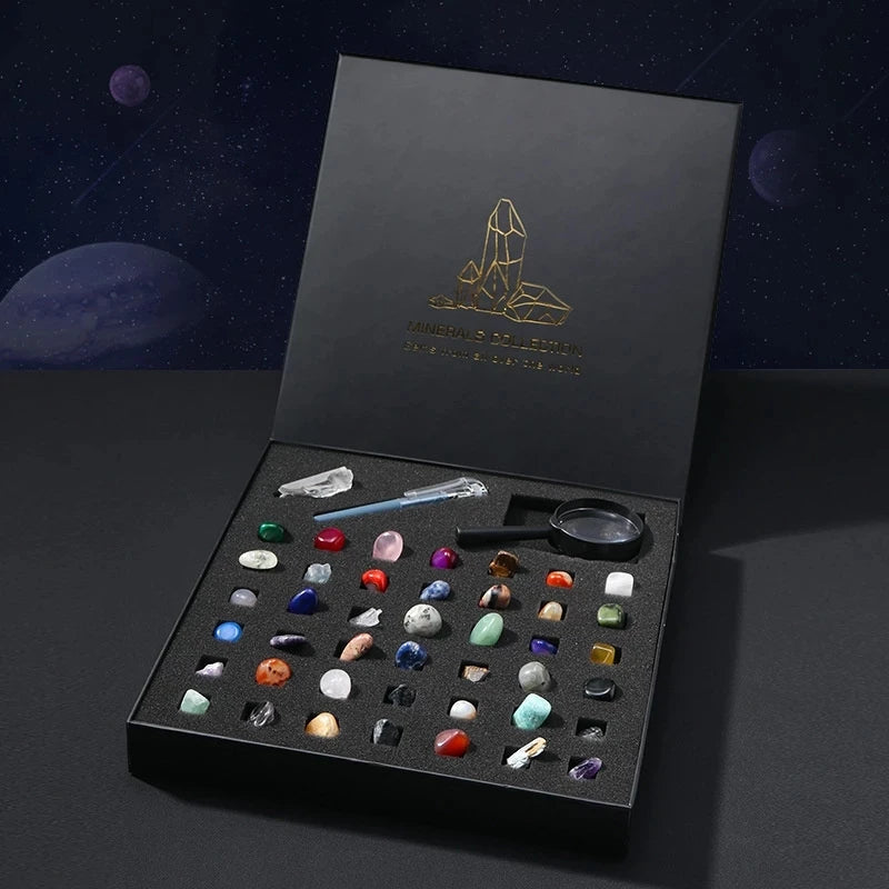 A black gift box containing a collection of natural crystal and mineral specimens, including various stones and a magnifying 