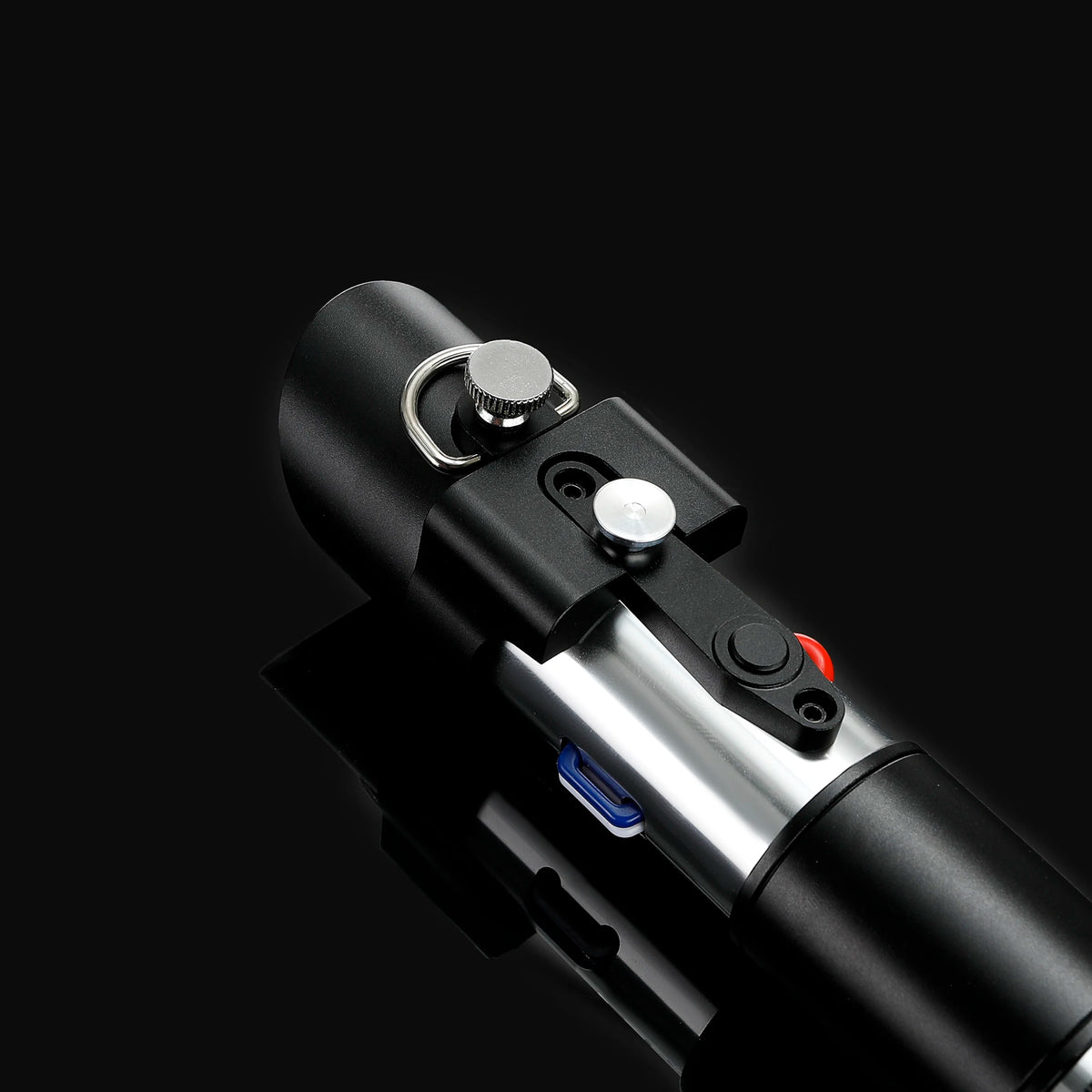 A close-up view of a black lightsaber hilt with silver accents and a red switch, set against a dark background.