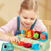 A young girl plays with a green pop-up animal toy featuring various colorful animals and Montessori learning elements.