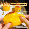 A hand squeezes a bright yellow pudding building block stress ball with a smooth, glossy texture.