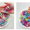 A hand holds a pile of colorful nylon hair ties in various shades of pink, purple, blue, and yellow.
