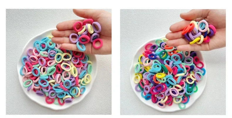 A hand holds a pile of colorful nylon hair ties in various shades of pink, purple, blue, and yellow.
