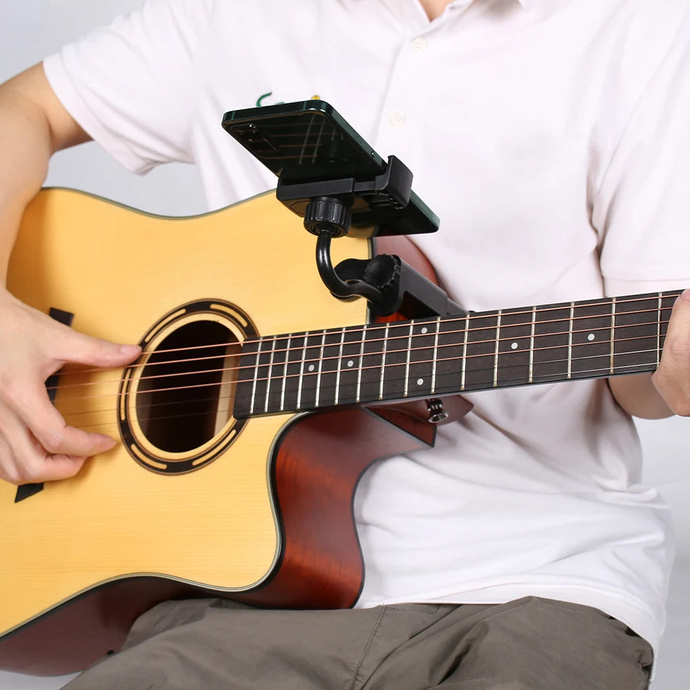 A person holds a guitar while using a hands-free phone holder clamp attached to the instrument's neck.