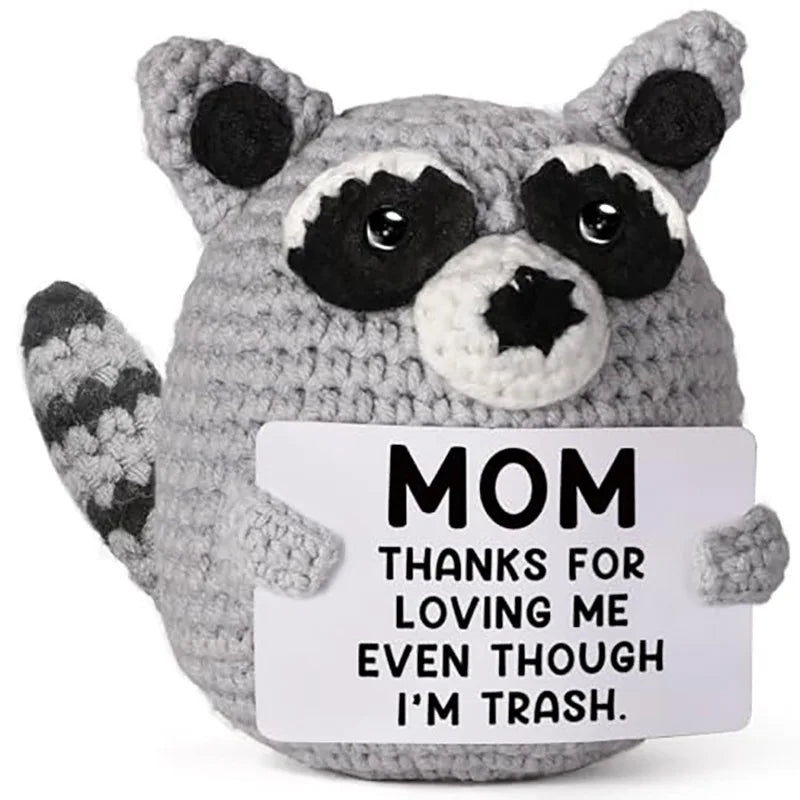 A gray handmade crochet animal plush doll with black markings and a sign that reads MOM THANKS FOR LOVING ME EVEN THOUGH I'M 