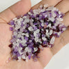 A handful of natural tumbled stone chips in shades of purple and clear quartz crystals.