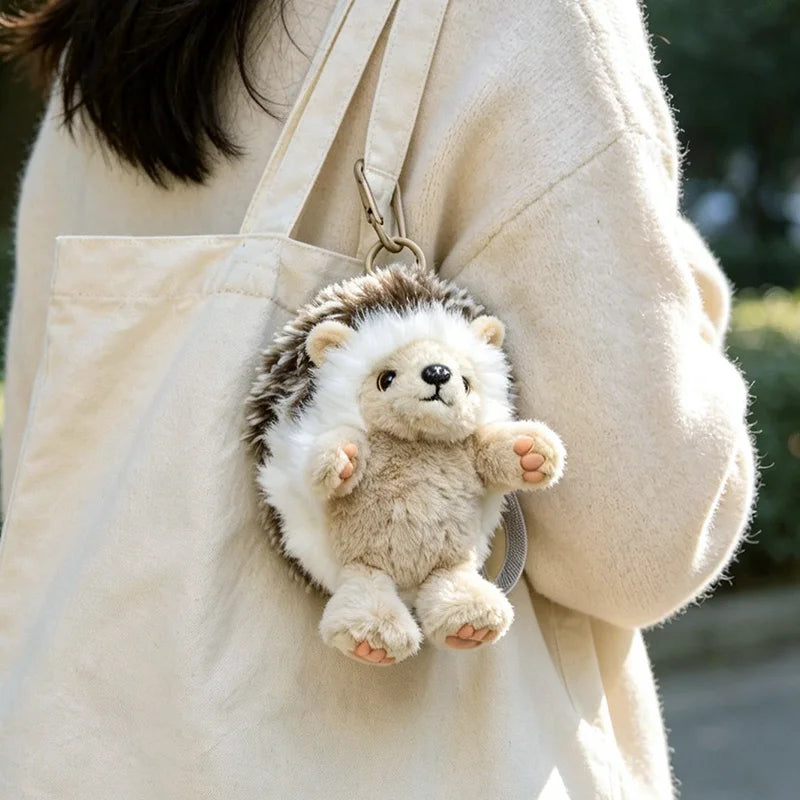 A small, fluffy hedgehog plush toy hanging from a strap on a light-colored canvas bag.