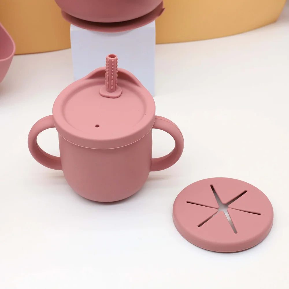 A pink silicone baby tableware set featuring a pot and lid, displayed on a white surface.
