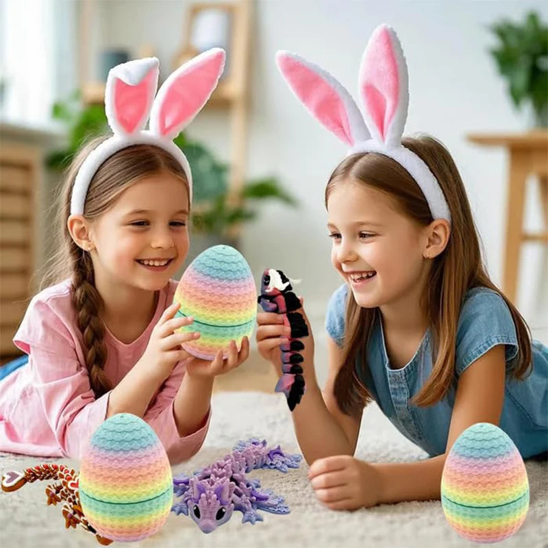 Two girls holding articulated dragon eggs with pink and green colors on a white blanket.