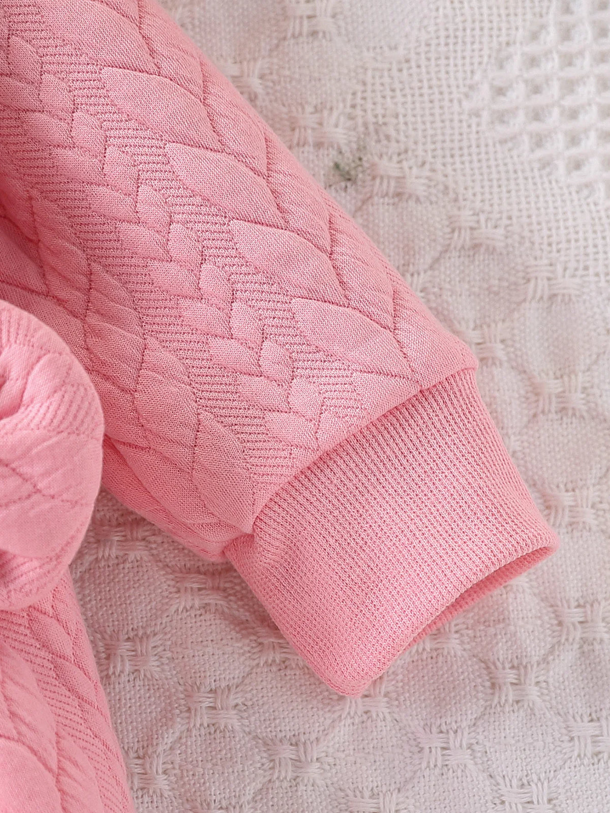 Pink quilted baby girl romper with a lace collar shown in a close-up view.