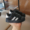 A pair of black and white Adidas sneakers with hook-and-loop closure held in a hand.