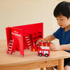 A young boy is playing with a red wooden fire brigade building set featuring ladders and a red vehicle.