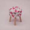 A round mini sofa and pillow set with a white fabric featuring pink floral patterns, supported by wooden legs.