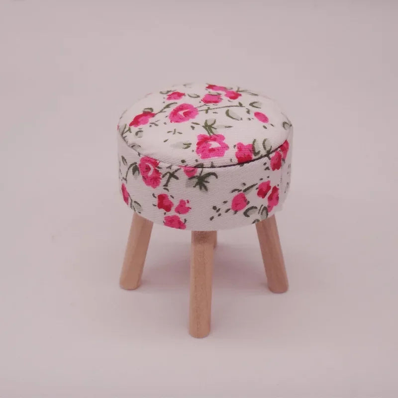 A round mini sofa and pillow set with a white fabric featuring pink floral patterns, supported by wooden legs.