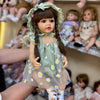 A realistic silicone vinyl toddler doll named Betty with long brown hair and a green dress sitting on a shelf.