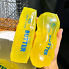 A hand holds a bright yellow butter squishy stress relief toy with the word BUTTER printed on it.