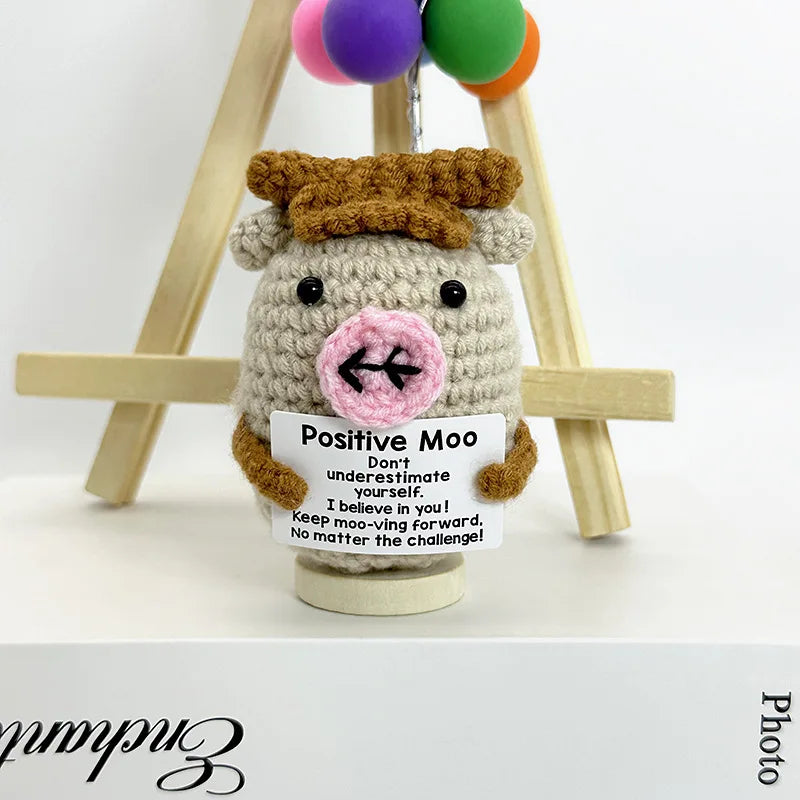 A handwoven crochet sheep ornament with brown wool and a pink face, displayed on a wooden easel.