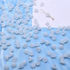 A collection of small, translucent white glass beads shaped like lily of the valley flowers scattered on a blue surface.