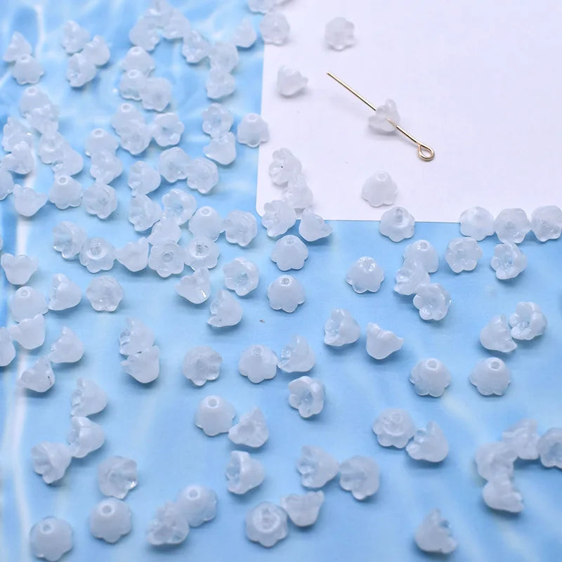A collection of small, translucent white glass beads shaped like lily of the valley flowers scattered on a blue surface.