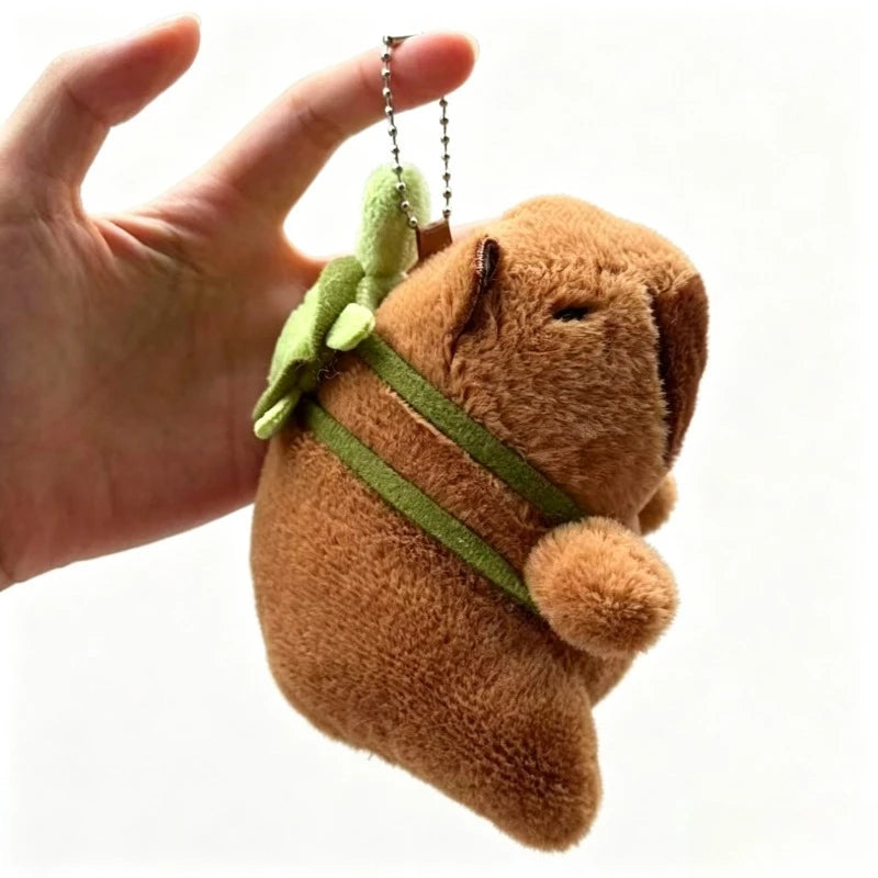 A brown capybara plush toy with a green ribbon and leaves, held in a person's hand.
