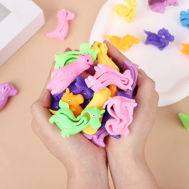 A hand holds a pile of colorful animal and dinosaur sensory stress bracelets for kids on a white surface.