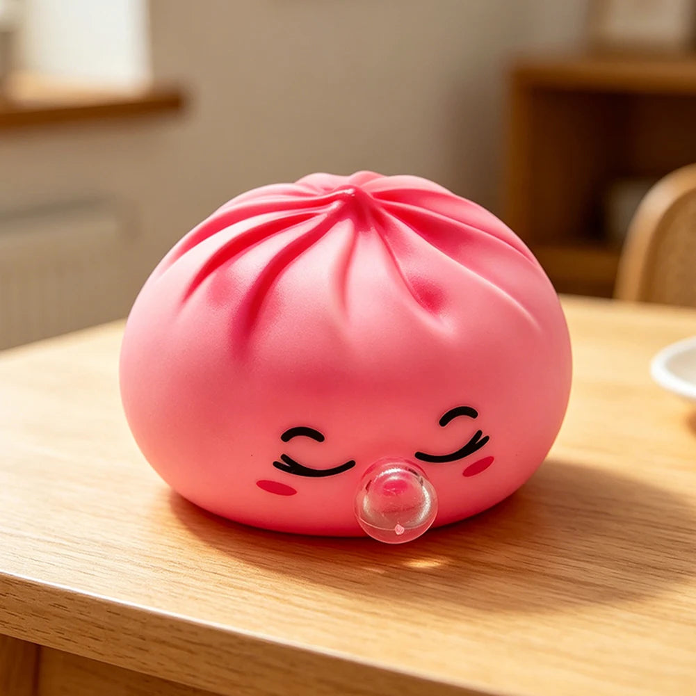 A pink, squishy dumpling-shaped stress relief toy with closed eyes and a clear bubble feature resting on a wooden surface.