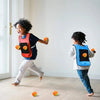 A young child is playing with a sticky dodgeball vest set indoors on a light wooden floor.