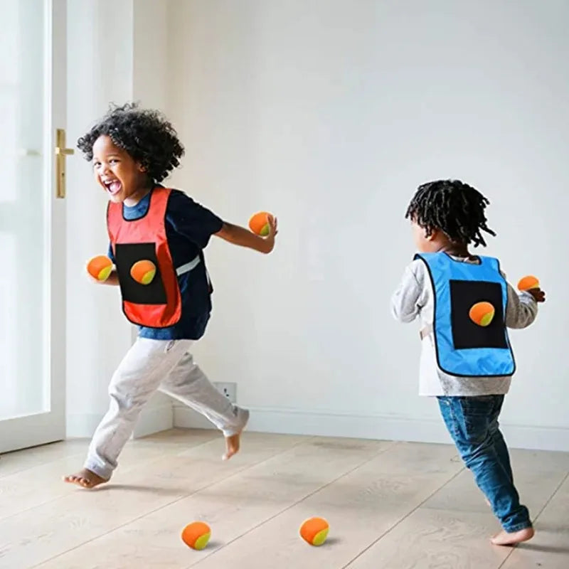 A young child is playing with a sticky dodgeball vest set indoors on a light wooden floor.
