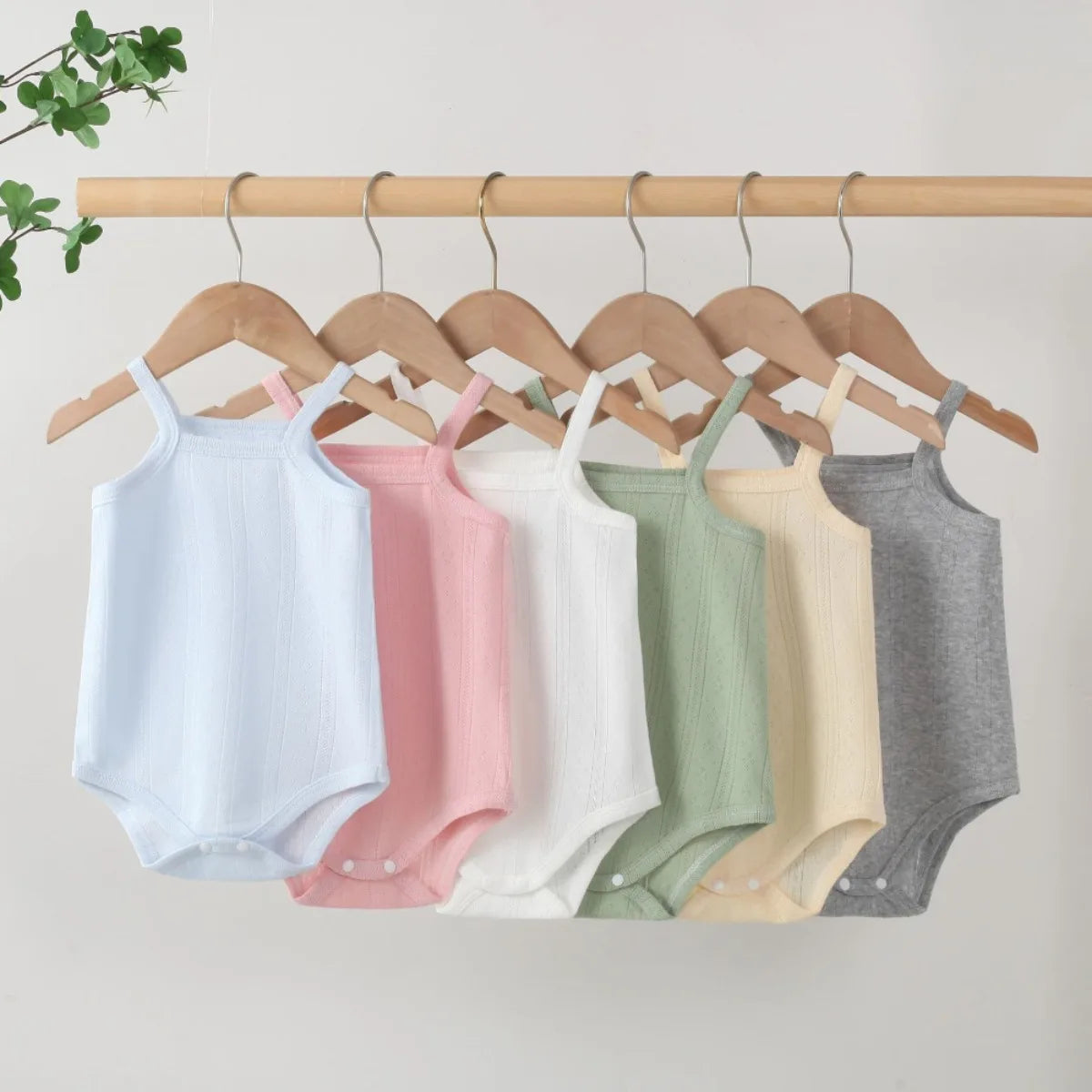 A collection of lightweight cotton strappy rompers in various pastel colors hanging from a wooden rack.
