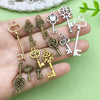 A hand holds various vintage key charms and pendants in gold and silver tones against a light green background.