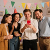 Four young adults smiling while looking at a red smartphone, with colorful pennant banners in the background.