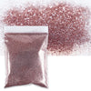 A package of fine holographic glitter powder in a rose gold color next to a loose pile of the same glitter.