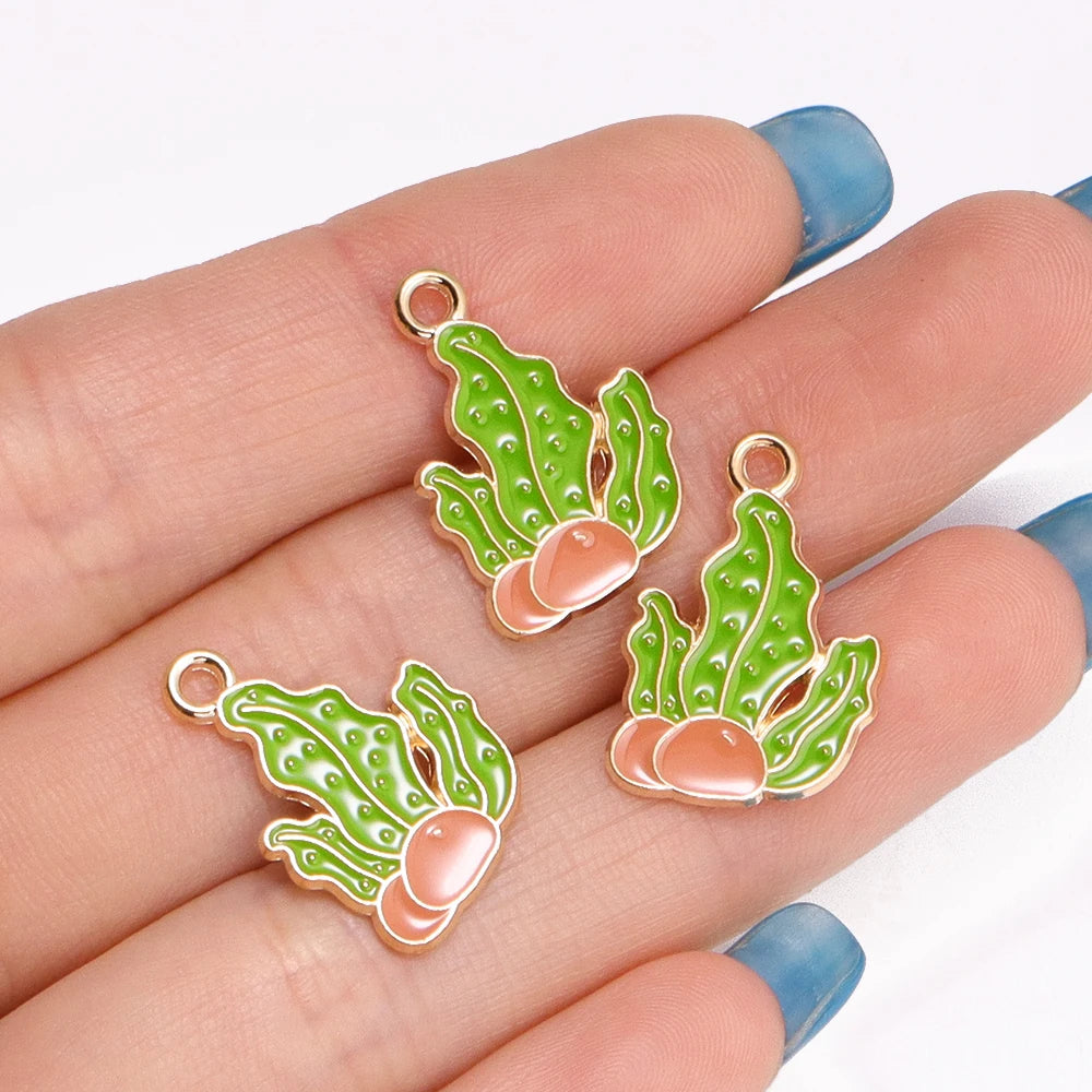 A hand holds several green enamel marine life charms for jewelry making