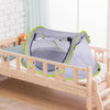 A light gray instant pop-up baby tent with green trim is placed on a wooden crib next to a teddy bear.