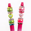 A vertical arrangement of pink and iridescent heart-shaped rhinestone flower charm beads on a pink stick.